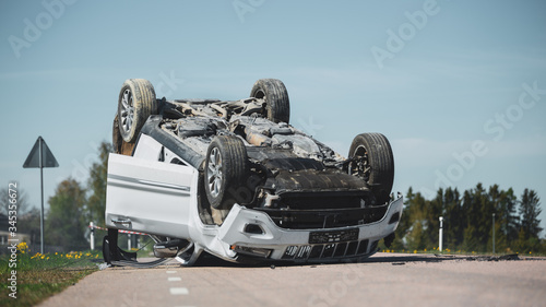 Horrific Traffic Accident, Rollover Smoking and Burning Vehicle Lying on its Roof in the Middle of the Road after Collision. Daytime Crash Scene with Severely Damaged Modern SUV Car.
