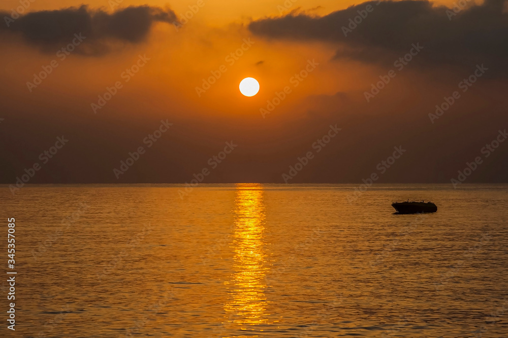 
Early sea morning, the sun is low above the horizon, a calm sea, a sunny path on the water, a lonely boat drifts.
