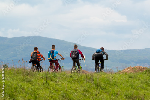 A group of four children riding a bicycle among nature against a mountain background. Тhey goes fishing through a green meadow.