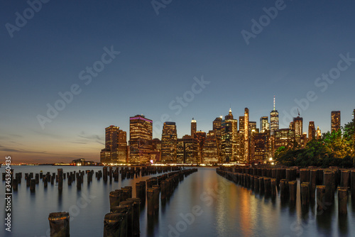 Blick   ber den East River nach Manhattan zur Abenddammerung in Langzeitbelichtung-im Vordergrund Holzpf  hle