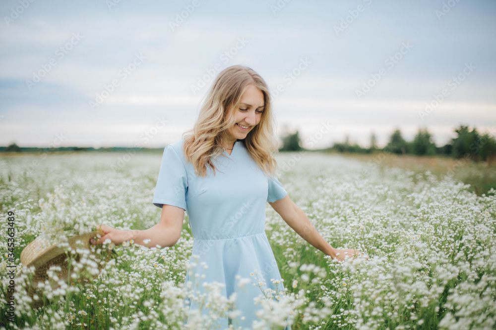 beautiful blonde girl in a field of daisies. wreath of wildflowers on his head. woman in a blue dress in a field of white flowers. charming girl with a bouquet of daisies. summer tender photo