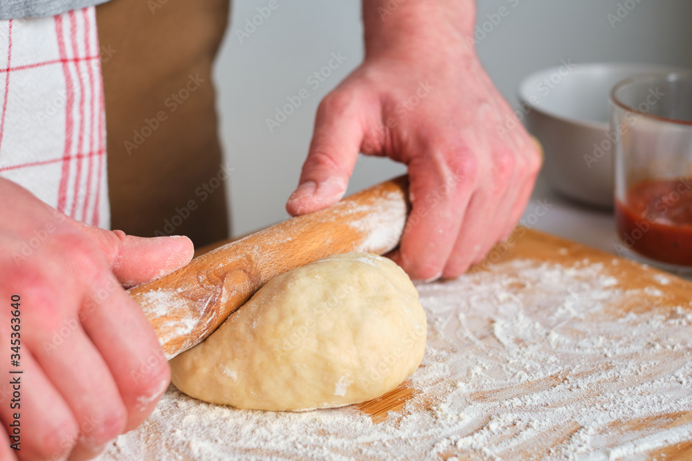 A man is preparing pizza dough. Men's hands in flour. Cooking homemade italian pizza. Preparation raw ingredients for baking. Fresh natural healthy food. Сulinary сhef kneading dough on kitchen table