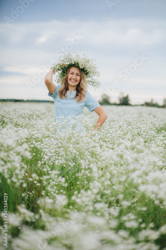 beautiful blonde girl in a field of daisies. wreath of wildflowers on his head. woman in a blue dress in a field of white flowers. charming girl with a bouquet of daisies. summer tender photo