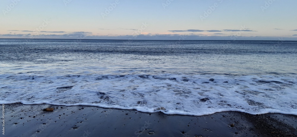 Sandy beach view with waves at sunset in Whitby, North Yorkshire