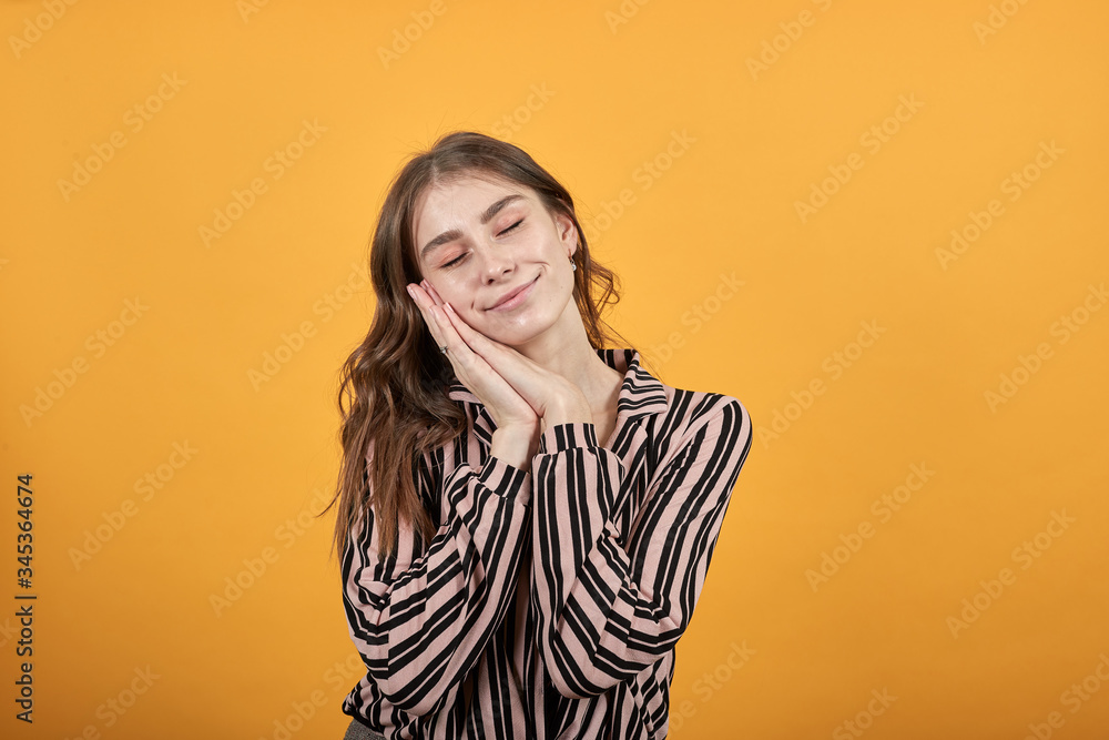 Cute Young Woman Light Brown In Striped Pink, Black Shirt On A Yellow Background, Sleepy Girl Rubs The Palms Of Her Hands Together And Sleeps Cute Young Woman Light Brown In Striped Pink, Black Shirt On A Yellow Background, Sleepy Girl Rubs The Palms Of Her Hands Together And Sleeps