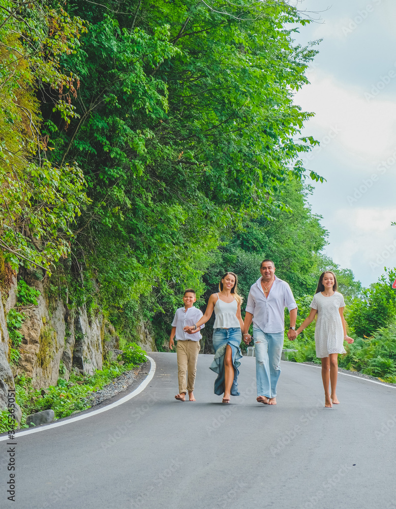 Cheerful, happy family, father, mother, son and daughter enjoying walk play outdoor near sea. Funny family in white clothes barefoot running on walkway. Green rocks at background. Cheerful, happy family, father, mother, son and daughter enjoying walk play outdoor near sea. Funny family in white clothes barefoot running on walkway. Green rocks at background.