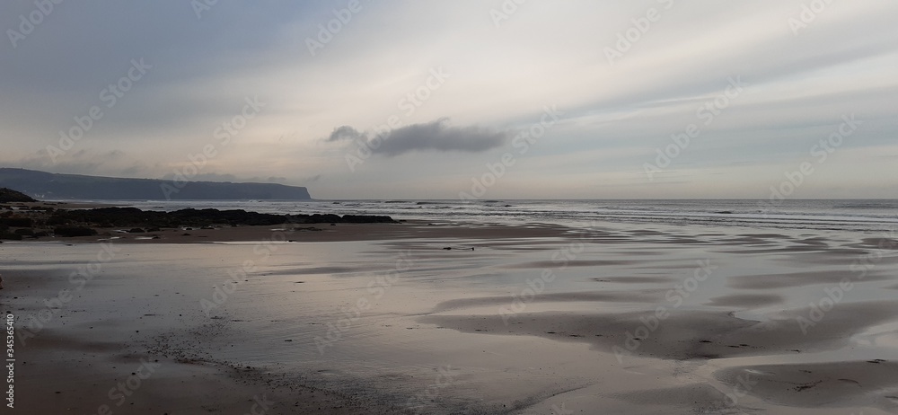 Obraz premium Sandy beach view with waves at sunset in Whitby, North Yorkshire