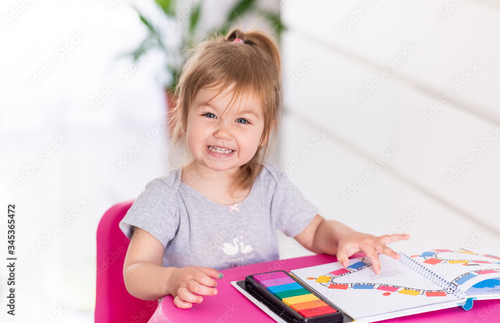 Concentrated cute 2year old girl is playing with stickers at home. Quarantine. Stay home. Indoor activities.Super emotional little girl looking in camera Concentrated cute 2year old girl is playing with stickers at home. Quarantine. Stay home. Indoor activities.Super emotional little girl looking in camera