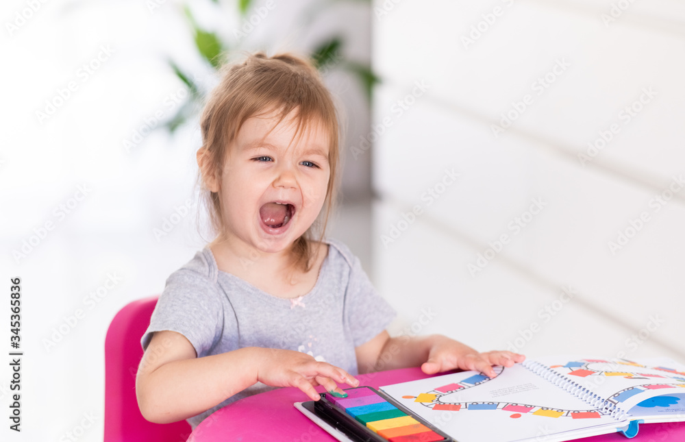 Concentrated cute 2year old girl is playing with stickers at home. Quarantine. Stay home. Indoor activities. Super emotional little girl Concentrated cute 2year old girl is playing with stickers at home. Quarantine. Stay home. Indoor activities. Super emotional little girl
