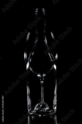 Silhouette of a transparent glass bottle with a glass of wine behind with black background