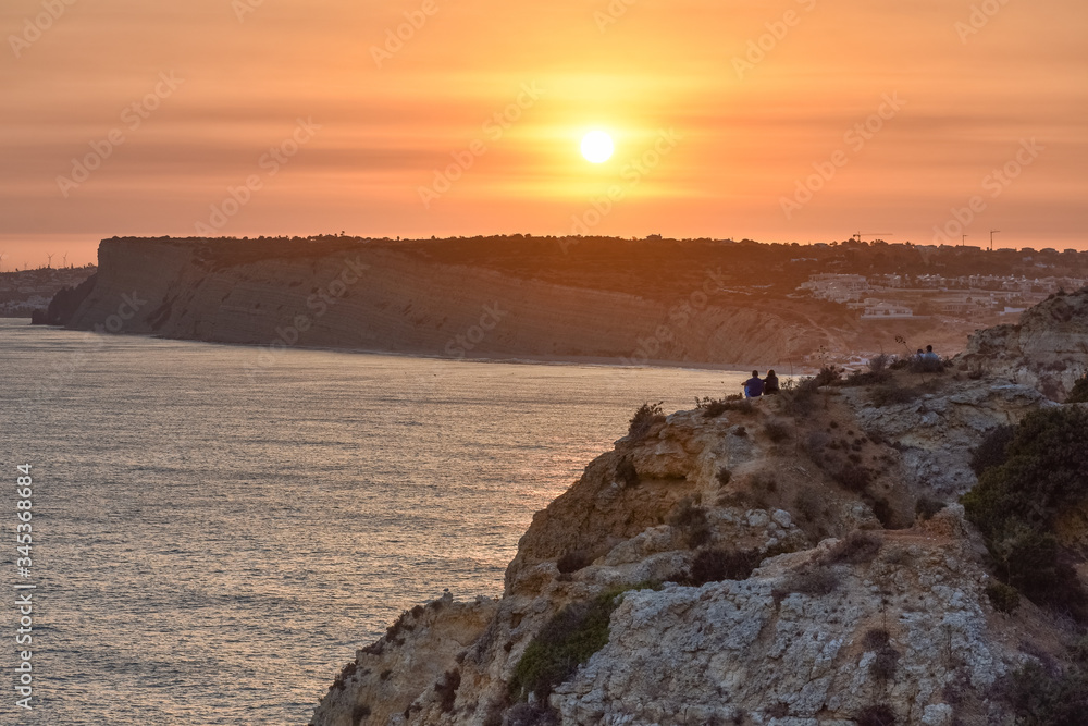People enjoying a Beautiful sunset over the cliffs of the beach. Concept of tourism and travel. Algarve, Portugal