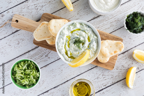 Photos A top down view of tzatziki dip garnished with lemon and dill and surrounded by ingredients used to make the dip