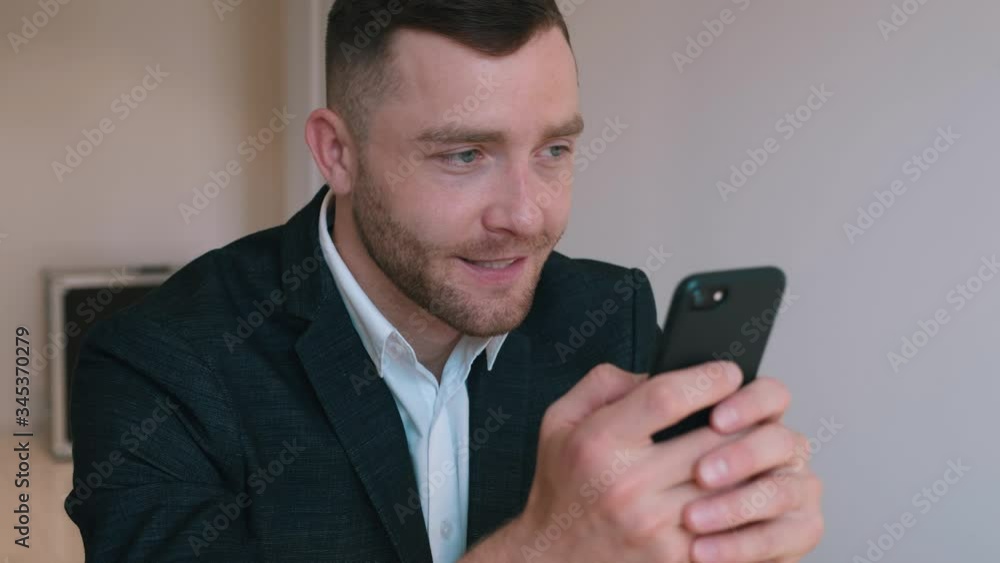 Confident Businessman in Formal Suit Sitting at His Desk in Home Office Using Smartphone, Browsing Through Internet, Social Media. Confident Businessman in Formal Suit Sitting at His Desk in Home Office Using Smartphone, Browsing Through Internet, Social Media.