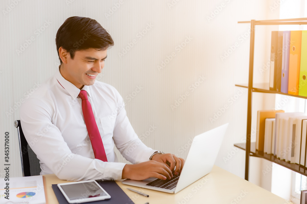 Fototapeta premium Young businessman analyzing data in office, sitting at his desk in the office with happy working. Attractive handsome working man using laptop computer. Businessperson get successful of business.