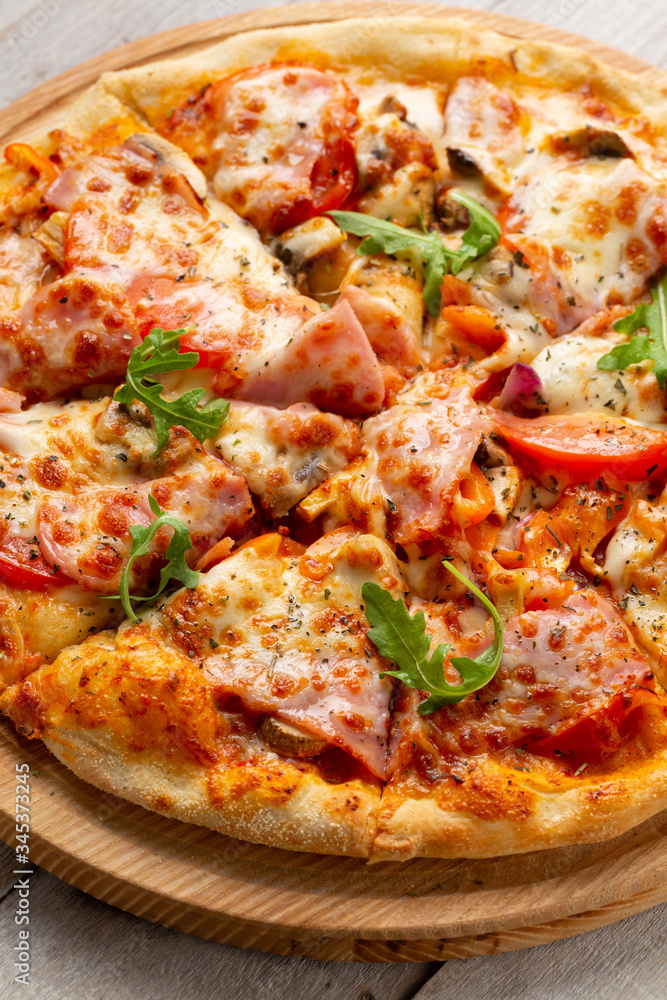 Tasty pizza with ham, mushrooms, tomatoes and arugula on wooden cutting board on white background. Tasty pizza with ham, mushrooms, tomatoes and arugula on wooden cutting board on white background.
