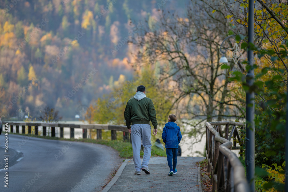 Father and son enjoy in walk by the road near forest in autumn