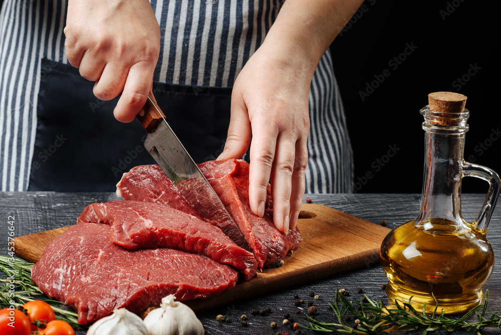 Woman cuts a piece of beef with a knife on a cutting board close-up.
