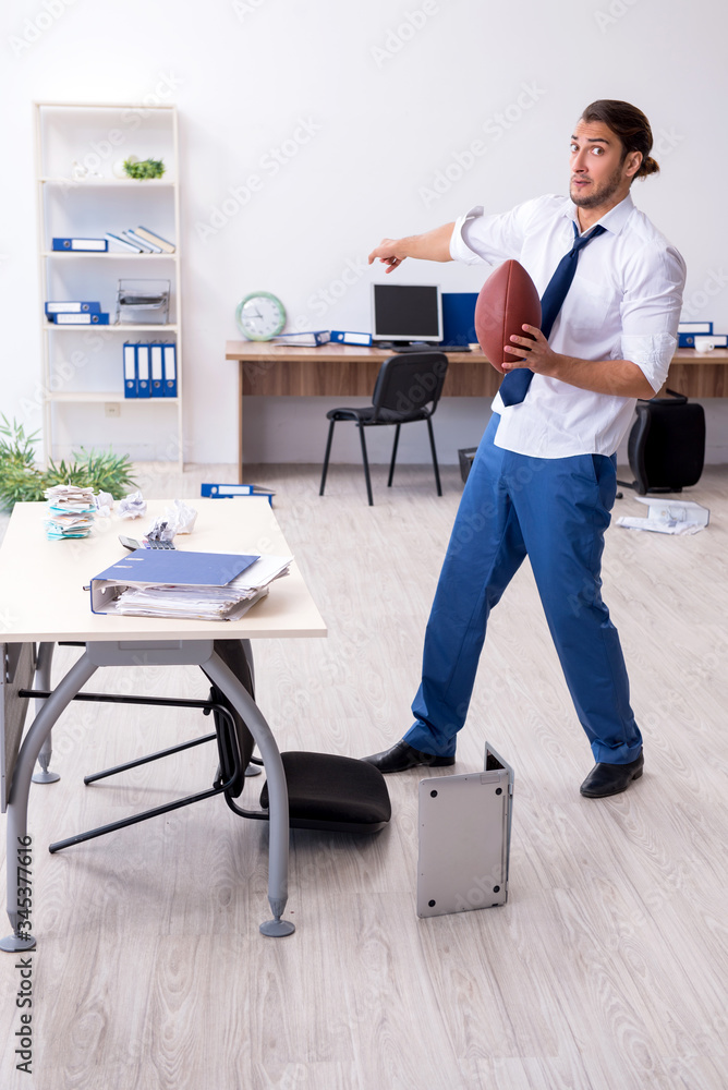 Young male employee throwing rugby ball in the office Young male employee throwing rugby ball in the office