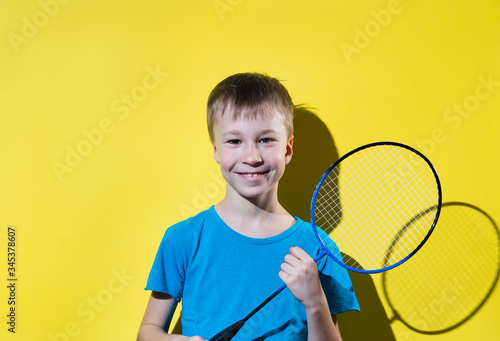 Happy boy with badminton racket isolated on yellow background.