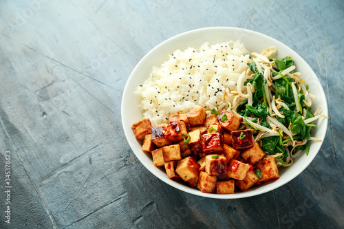 Fried tofu in sweet chilli glaze served with rice, steamed spinach and beansprouts in white bowl. Vegetable healthy food