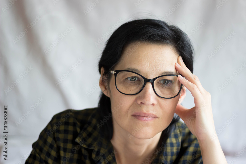 A pretty middle-aged brunette with glasses looks thoughtfully at the camera. A surprised, questioning look. Emotions. A pretty middle-aged brunette with glasses looks thoughtfully at the camera. A surprised, questioning look. Emotions.