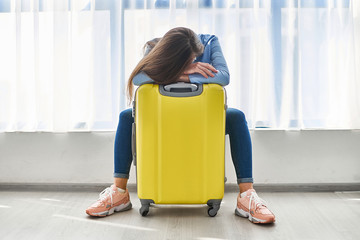 Woman traveler with yellow suitcase affected by flight delay and cancelled travel and vacation holiday. Travel ban and traveling troubles