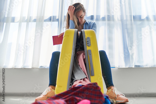 Upset woman traveler affected by flight delay and cancelled travel and vacation weekends holiday. Travel ban and traveling troubles. Problems while packing clothes in a suitcase photo