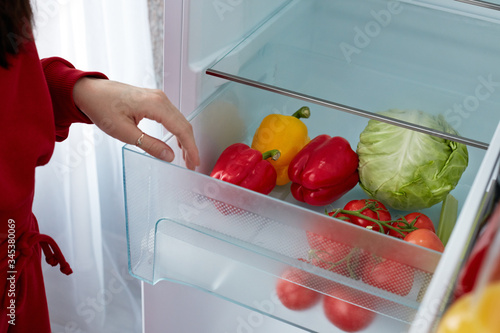 Close-up Of Young Woman Searching For Food In The Fridge. Red and yellow pepper, tomatoes and cabbage in fridge. Donation concept.