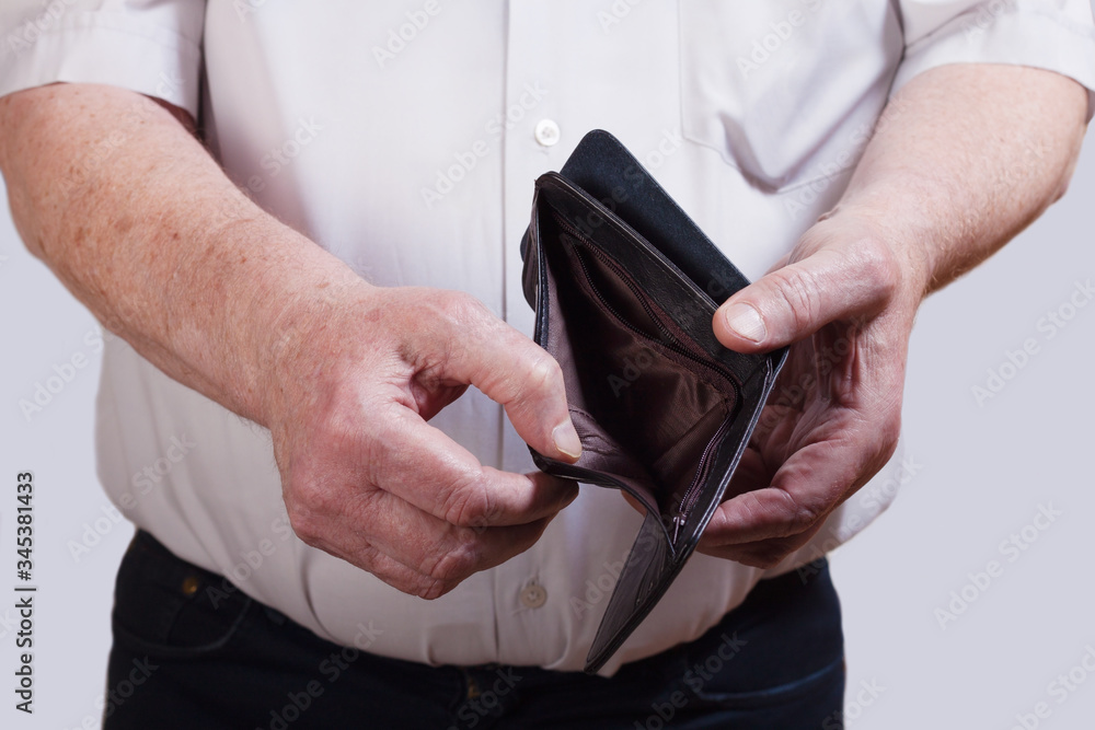 An elderly man holds an empty wallet in his hands. The concept of poverty, job loss, dismissal, retirement, price increases.