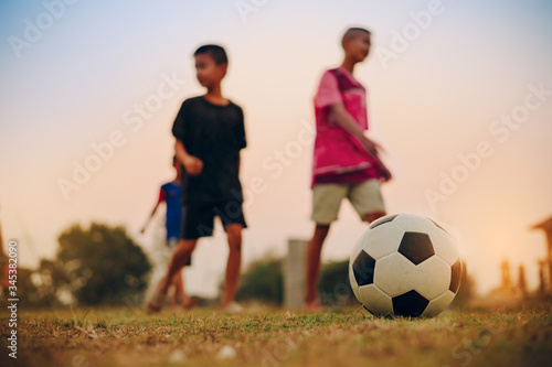 Action sport outdoors of kids having fun playing soccer football for exercise in community rural area under the twilight sunset sky.