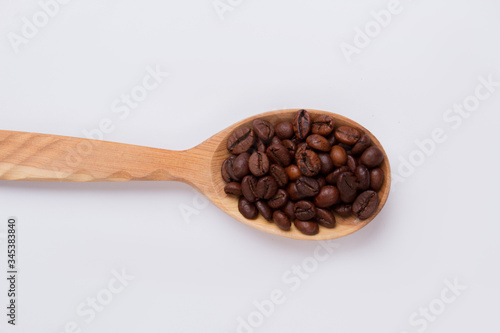Rustic wooden spoon filled with coffee beans. White isolated background.