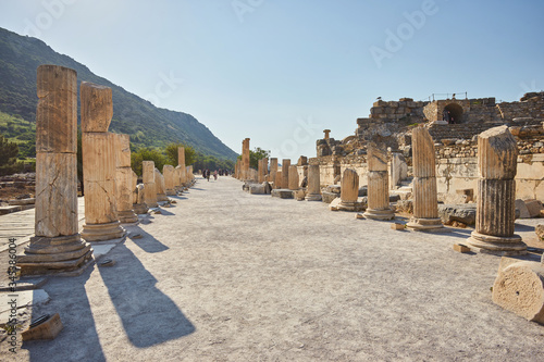 marble alley with columns leading to the Celsus Library in ancient greek city of Ephesus with mountains and clear blue sky at background with single small cloud over the Celsus Library
