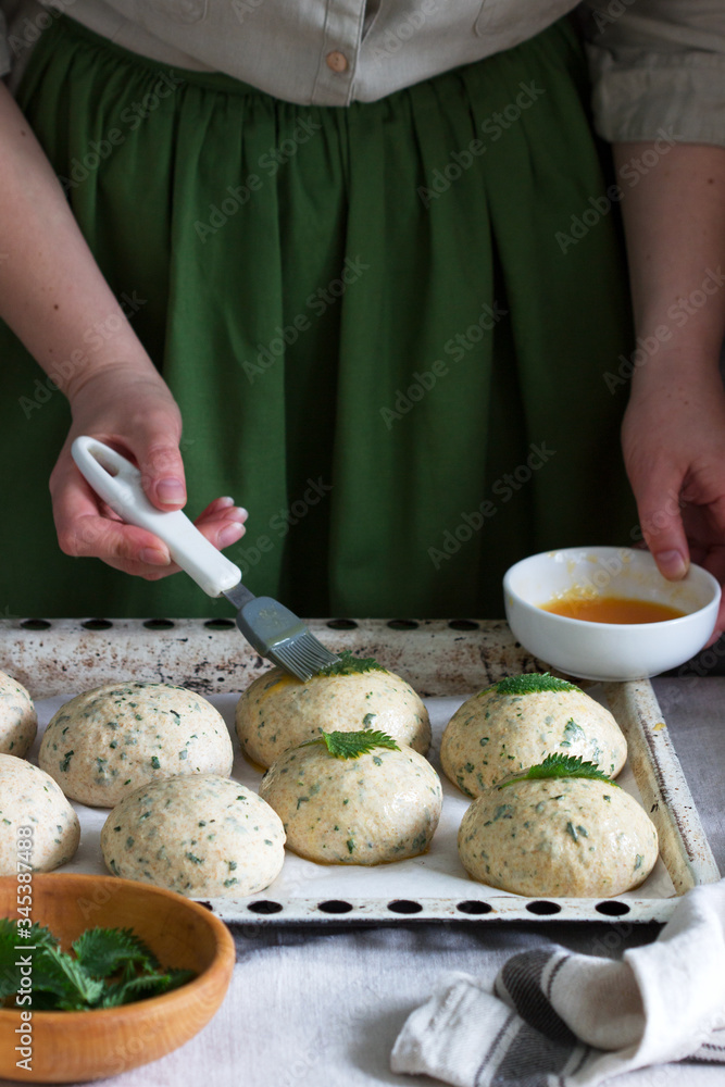 A woman is preparing buns from yeast dough with nettles. Rustic style.