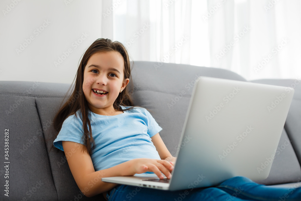 Naklejka premium Head shot close up portrait of happy small pupil learning at home. Smiling little child girl enjoying doing lessons in living room. Smart kid schoolgirl looking at camera, studying remotely online.