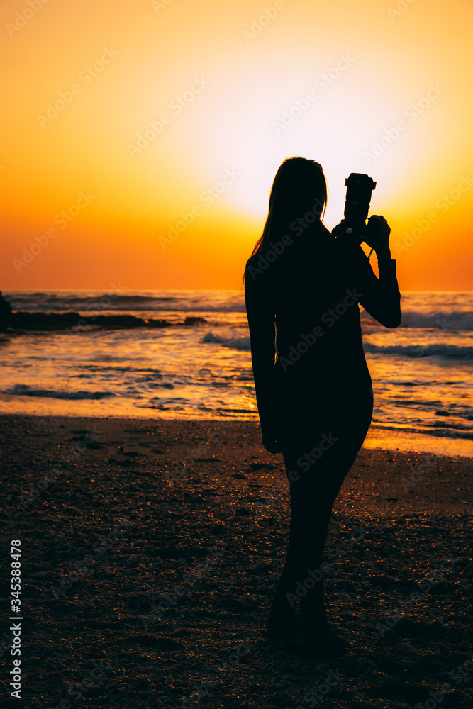 Woman photographer silhouette from back on sea sunset beach in the evening. Golden sunset on Mediterranean Sea with nice woman with camera. Meeting the end of the day by the sea