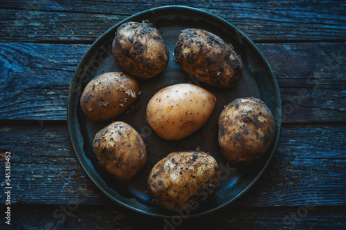 Young raw fresh clean and dirty farm potatoes in a plate on an old wooden table top view