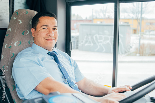 young smiling hispanic bus driver is holding a wheel, looking at the road.