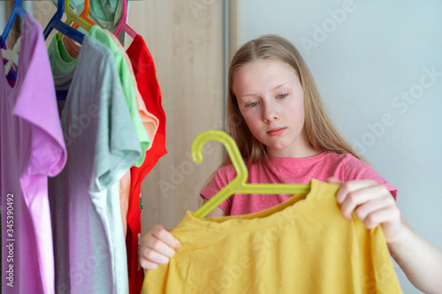 a girl staying near wardrobe and holds an old t-shirt with an elongated neck, sorting things for re-use