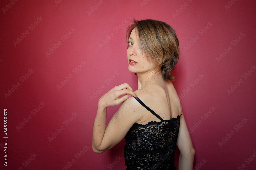 Young woman with short hair dressed in black lace bustier and blue jeans is posing in the studio on bright pink background Young woman with short hair dressed in black lace bustier and blue jeans is posing in the studio on bright pink background
