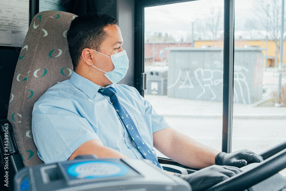 Fototapeta premium young hispanic man bus driver has blue medical protection mask and black gloves and looks at the road.