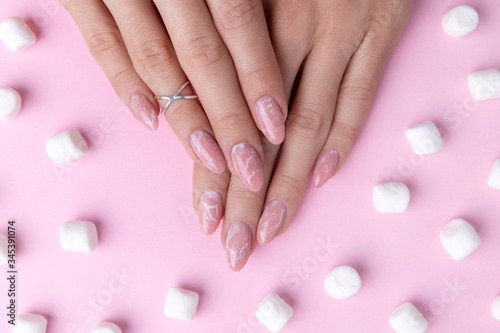 Womans hands with trendy marble manicure with marshmallows