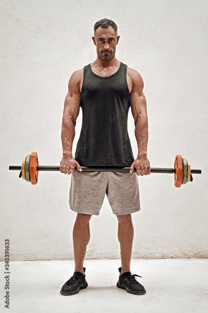 Strong and sportive fitness trainer holding a barbell isolated in a studio Strong and sportive fitness trainer holding a barbell isolated in a studio