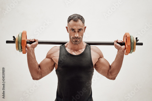 Close-up photo of a sportsman, flexing with a barbell in a bright studio