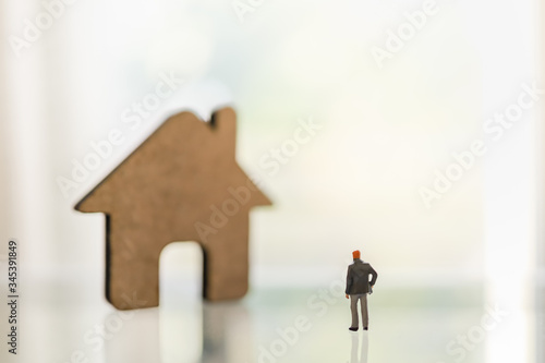 Business, Shelter in Place, Stay and Work at home and family Concept for Coronavirus 2019 (COVID-19). Businessman miniature figure people standing with wooden house icon on table with copy space.