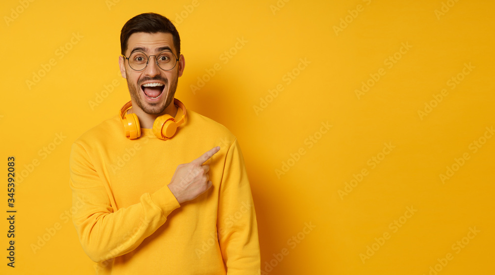 Horizontal banner of surprised man feeling shocked about beneficial commercial offer, pointing to copy space on right, screaming WOW, isolated on yellow background