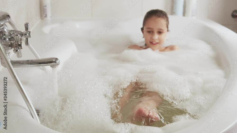 Close-up of a pretty little girl squishes feet in a bathtub full of foam. Hygiene and Baby Care Concept, HD still video camera, 4x slow motion.