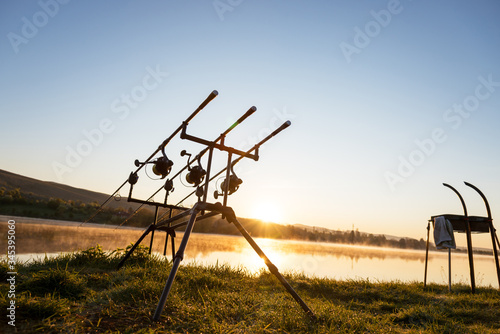 Carp fishing rods with carp bite indicators and reels set up on rod pod near lake river. Fishing during sunset.