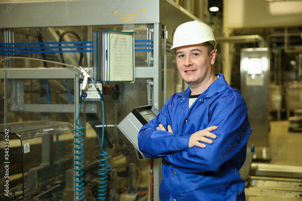 factory worker on the background of the equipment control panel at the factory. the factory engineer looks at camera factory worker on the background of the equipment control panel at the factory. the factory engineer looks at camera