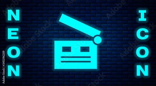 Glowing neon Movie clapper icon isolated on brick wall background. Film clapper board. Clapperboard sign. Cinema production or media industry.  Vector Illustration