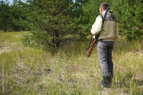 standing hunter with rifle in summer forest